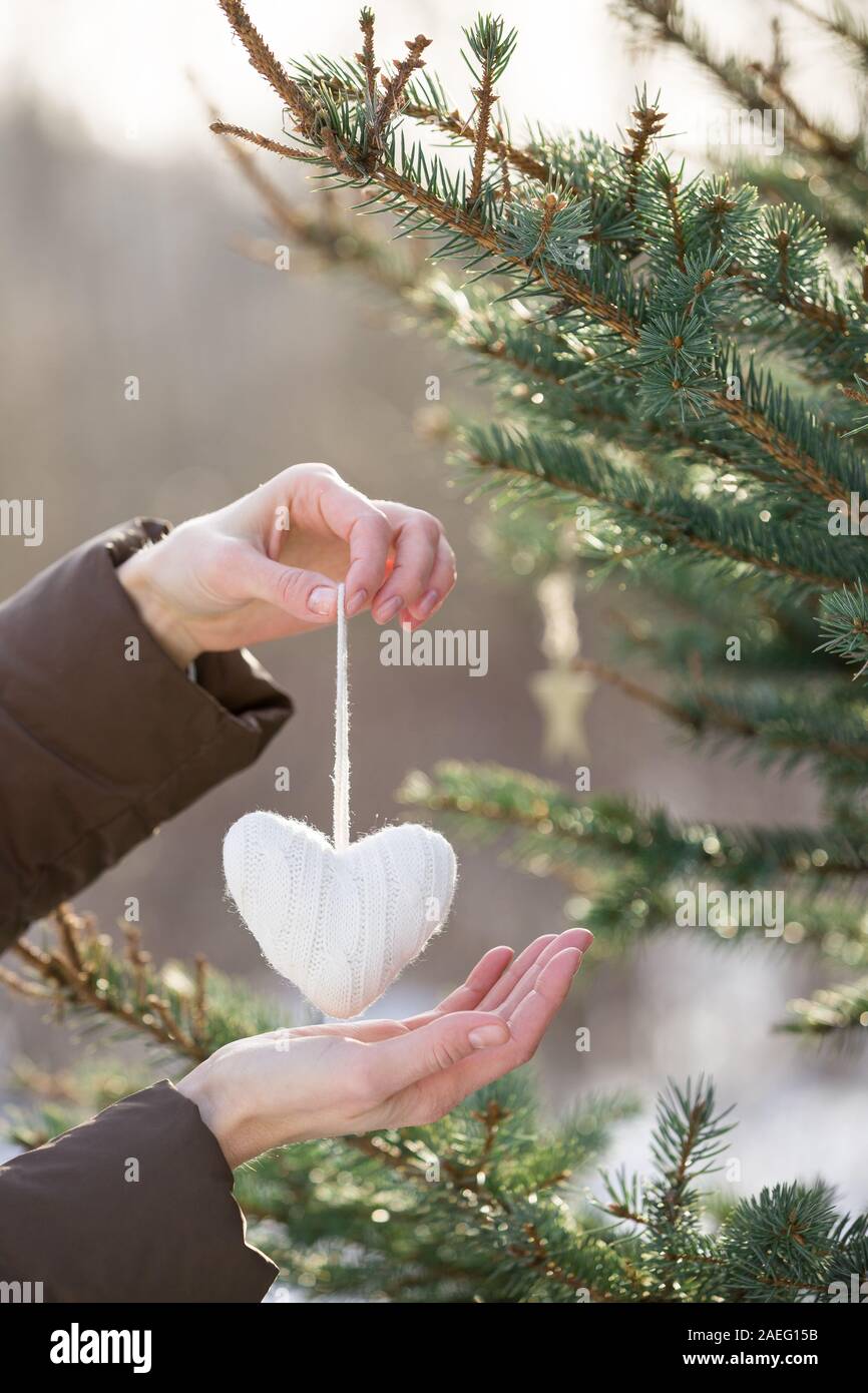 Close up of woman's hands decorating Christmas Tree avec coeur en tricot blanc à l'extérieur. Présente un décor et des éléments. Vacances d'hiver et de concept. Banque D'Images