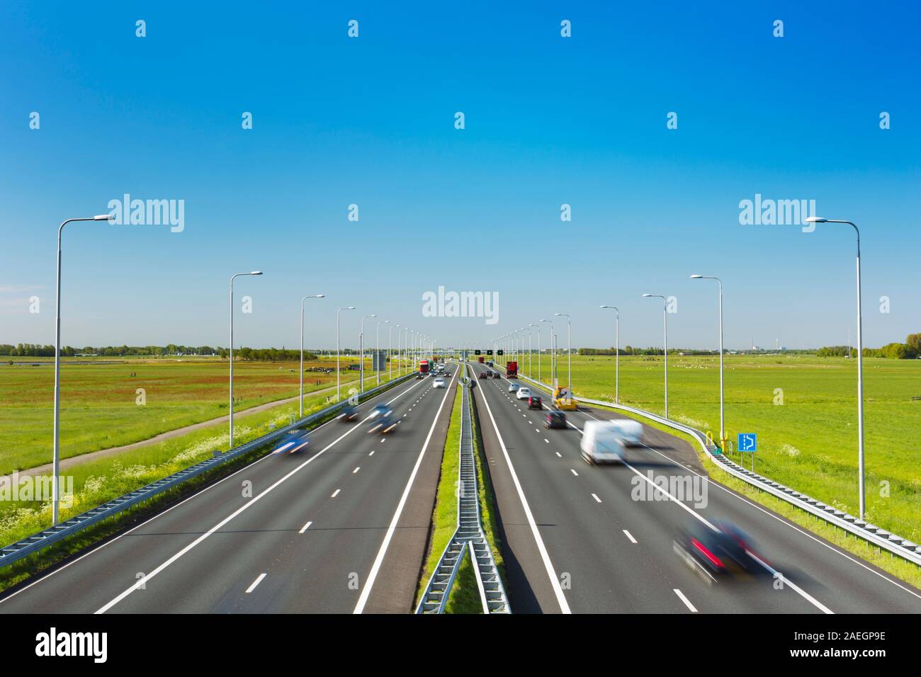 Une route avec un trafic à travers champs herbeux sur une journée ensoleillée dans les Pays-Bas. Banque D'Images