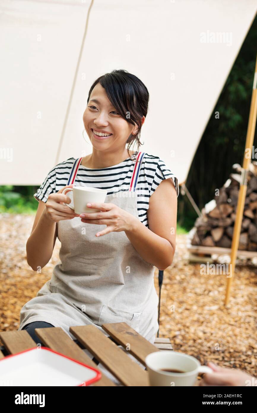 Smiling Japanese woman sitting outdoors à une table, boire de tasse de café. Banque D'Images