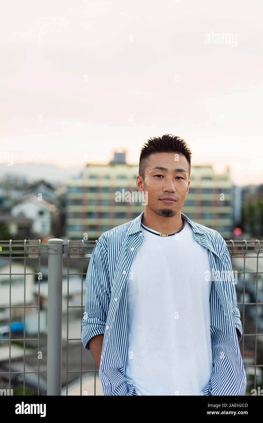 Jeune homme japonais debout sur un toit dans un milieu urbain, looking at camera. Banque D'Images
