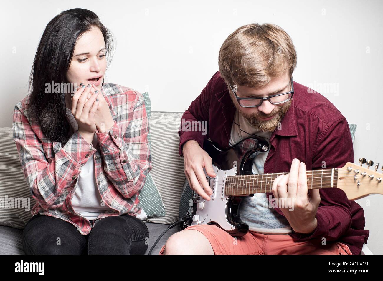 Jeune femme avec inquiétude et l'admiration à l'écoute que son petit ami joue la guitare électronique. Banque D'Images