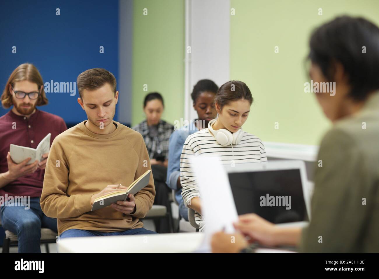Groupe multiethnique de jeunes gens assis et écrit dans des carnets tout en enseignant la lecture d'une conférence Banque D'Images