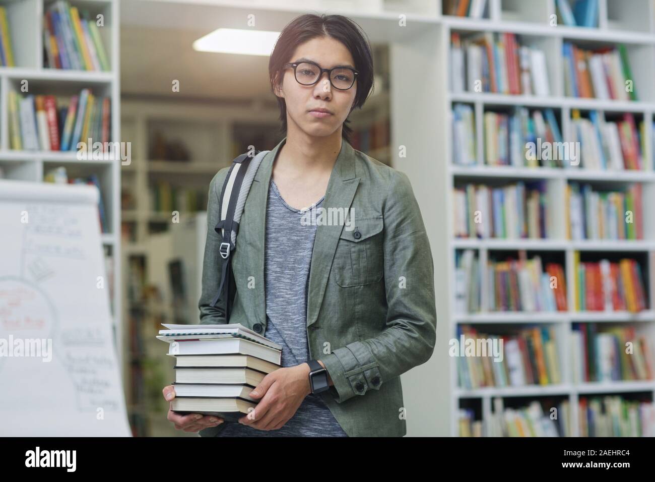 Portrait of Asian jeune étudiant de lunettes holding tas de livres et looking at camera il vient à la bibliothèque Banque D'Images
