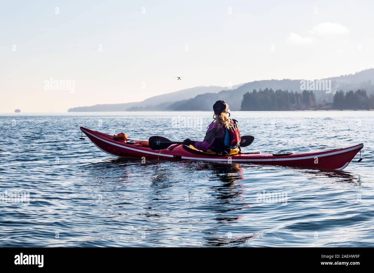 Un kayakiste de mer femelle regarder comme une mer avion atterrit juste au sud de Ganges Harbour, Salt Spring Island, en Colombie-Britannique, Canada. Banque D'Images