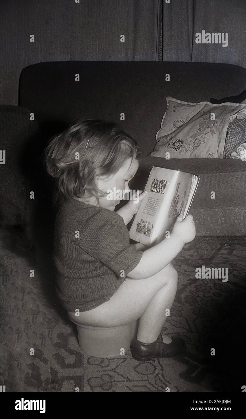 années 1950, historique, un enfant en bas âge assis sur un pot lisant un livre d'histoire. Banque D'Images