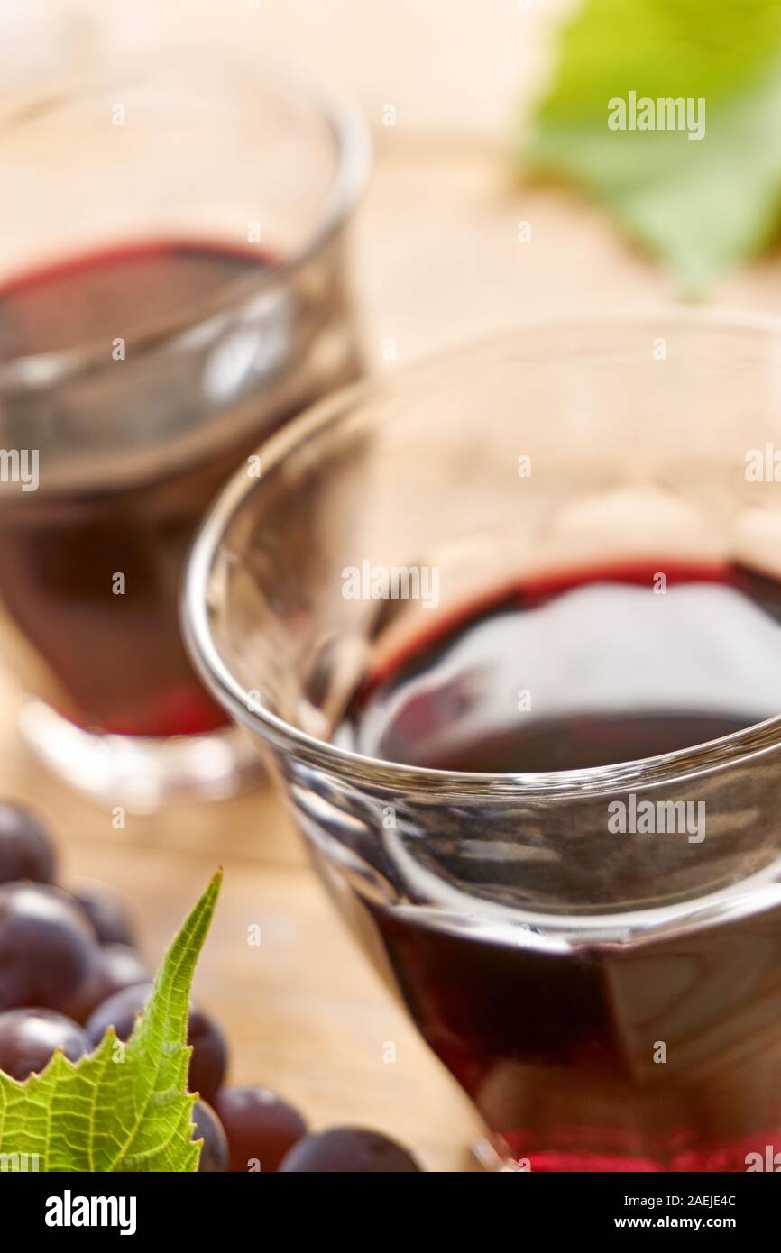 Deux verres à vin sans pied sur une table remplie de vin rouge, le raisin bleu et vert feuilles de raisin. L'angle vertical dutch avec focus sélectif, Banque D'Images