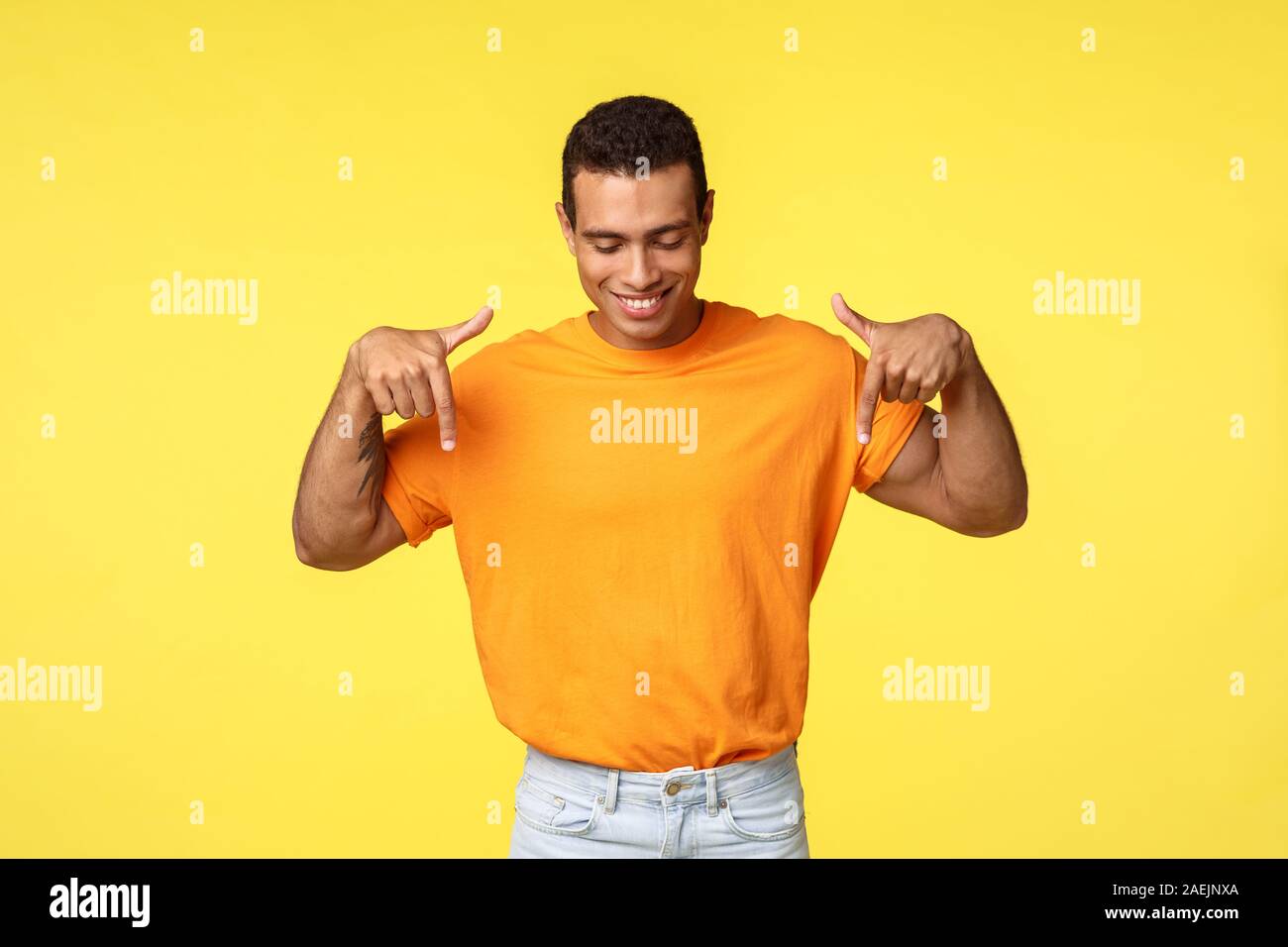 Convaincu guy masculin avec coupe sombre court, porter un tee-shirt orange  pointant vers le bas, et à la contempler une bonne promo et souriant  heureux, trouvé ce que Photo Stock - Alamy