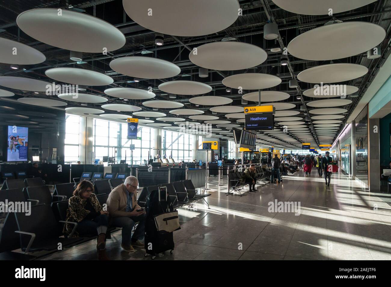 Les gens attendent à l'aéroport de portes à la borne 5, de l'aéroport Heathrow de Londres. Les disques de décoration décorer le plafond. Banque D'Images