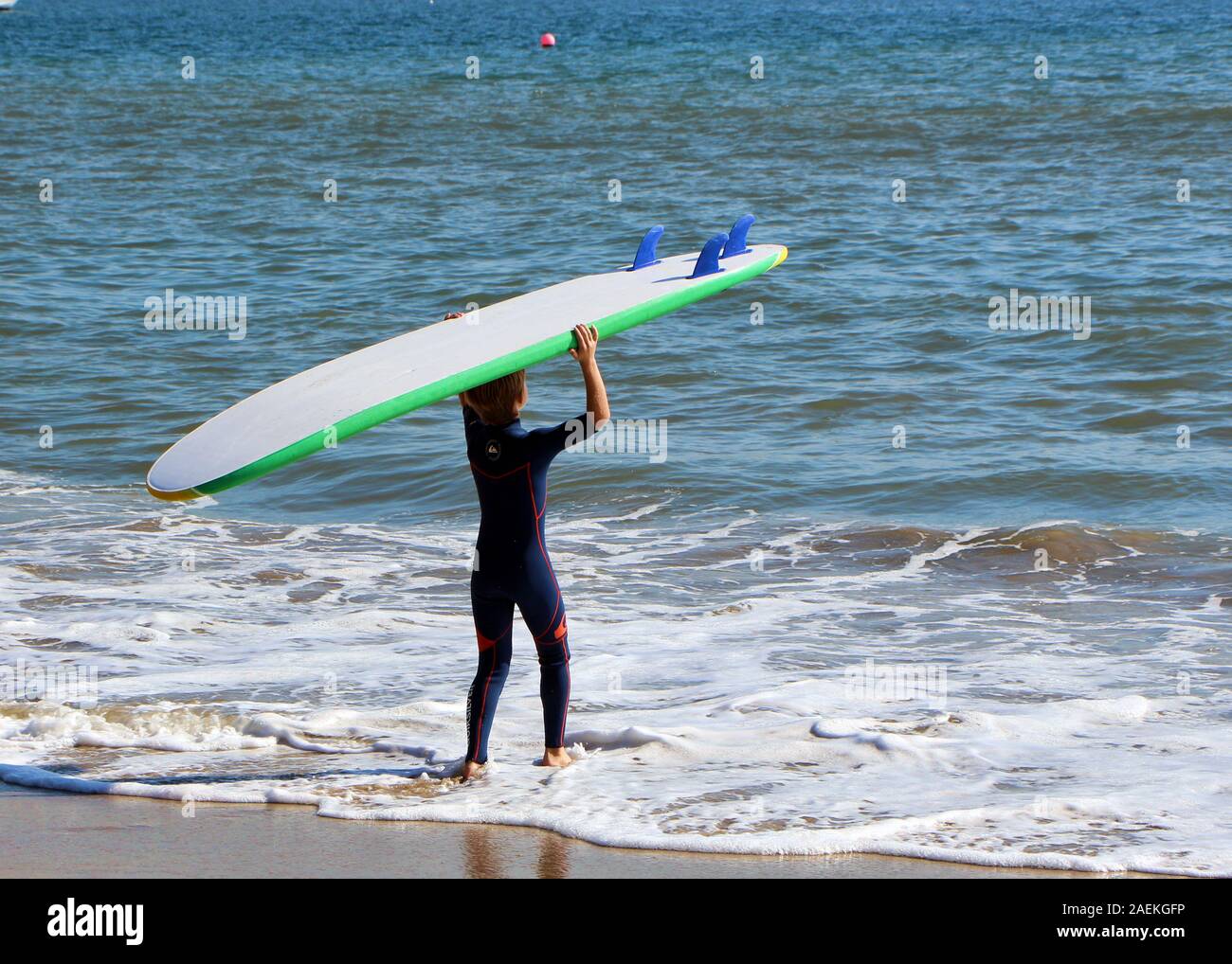 Un garçon va surfer sur la plage. Banque D'Images