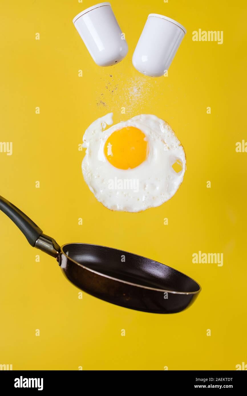 L'heure du petit-déjeuner. Un œuf frit et une poêle avec salières léviter dans l'air sur un fond jaune Banque D'Images