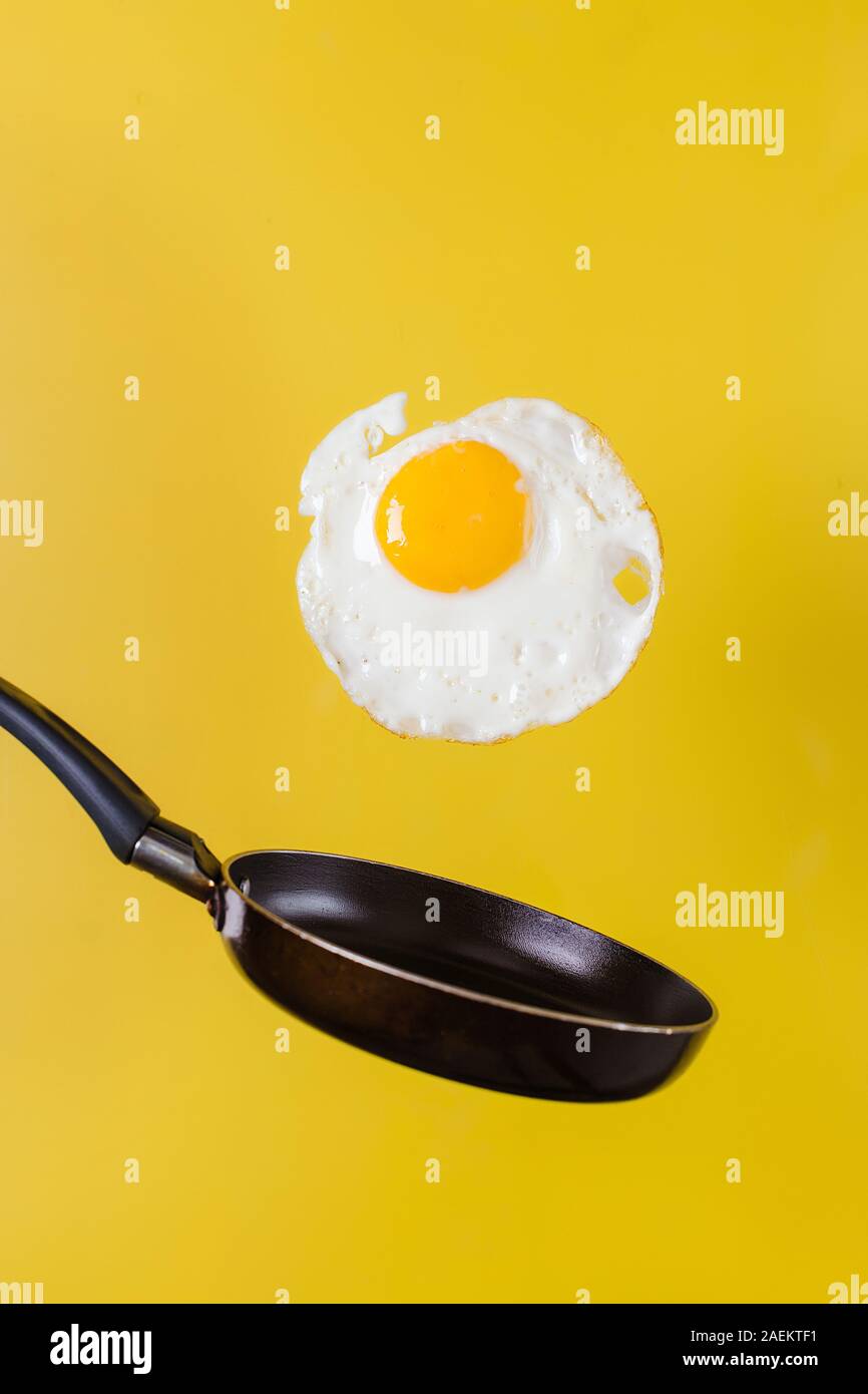 L'heure du petit-déjeuner. Un œuf frit et une poêle faire léviter dans l'air sur un fond jaune. Banque D'Images