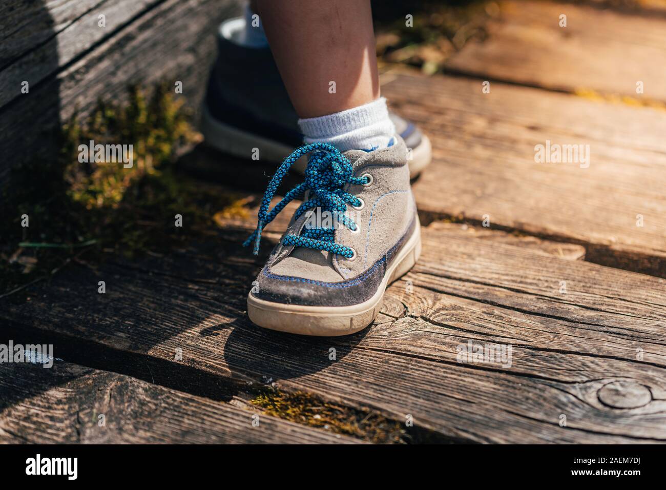 Chaussure de randonnée bleu et gris d'un jeune petit enfant sur une planche  en bois d'un pont dans les Alpes en Allemagne avec le soleil qui brille sur  une journée d'été Photo