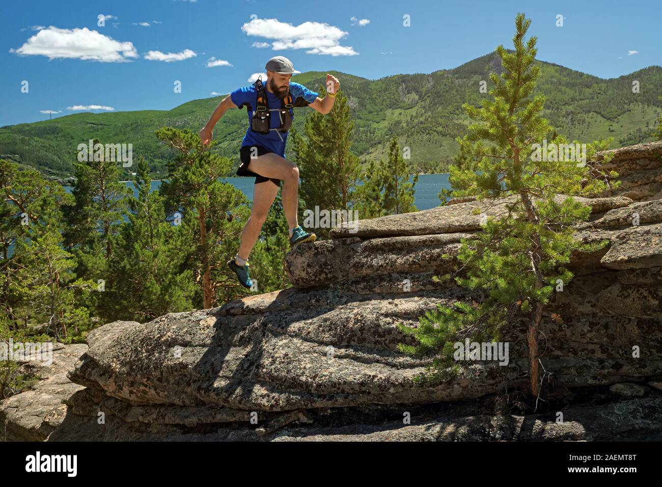 Runner l'ascension d'une roche. L'athlète exécute sur les rochers dans les montagnes. Le trail de plein air en journée ensoleillée. L'homme en bleu t-shirt et short noir train Banque D'Images