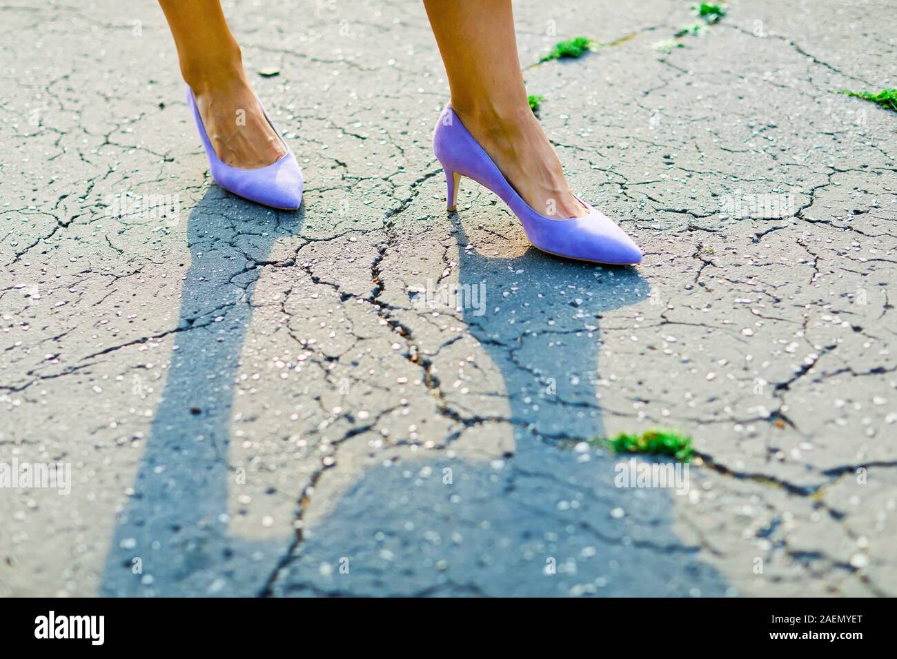 Pieds de femme violet portant des talons hauts, des chaussures élégantes sur surface fissurée Banque D'Images