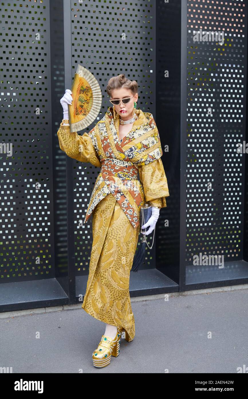 MILAN, ITALIE - 22 septembre 2019 : Femme avec robe kimono marron et doré et le ventilateur à la main avant d'Gucci fashion show, Milan Fashion Week street style ? Banque D'Images