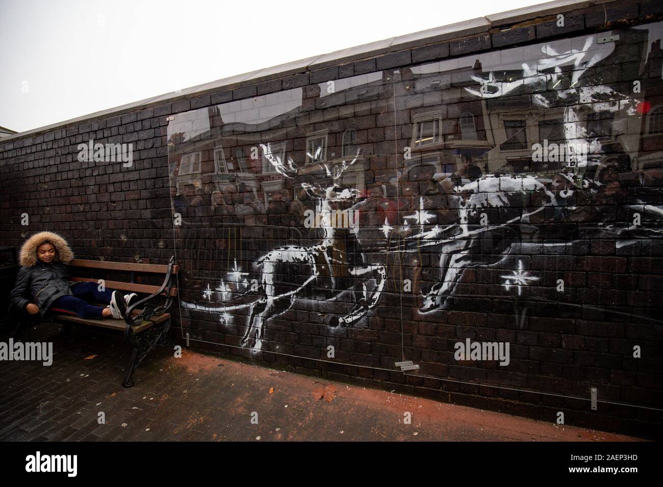Draps perspex ouvriers pour protéger une nouvelle illustration Banksy à Birmingham's Jewellery Quarter après qu'elle a été vandalisée jours après son apparition. La murale représentant deux rennes peints sur un mur de briques qui semble tirer le long d'un banc. Banque D'Images