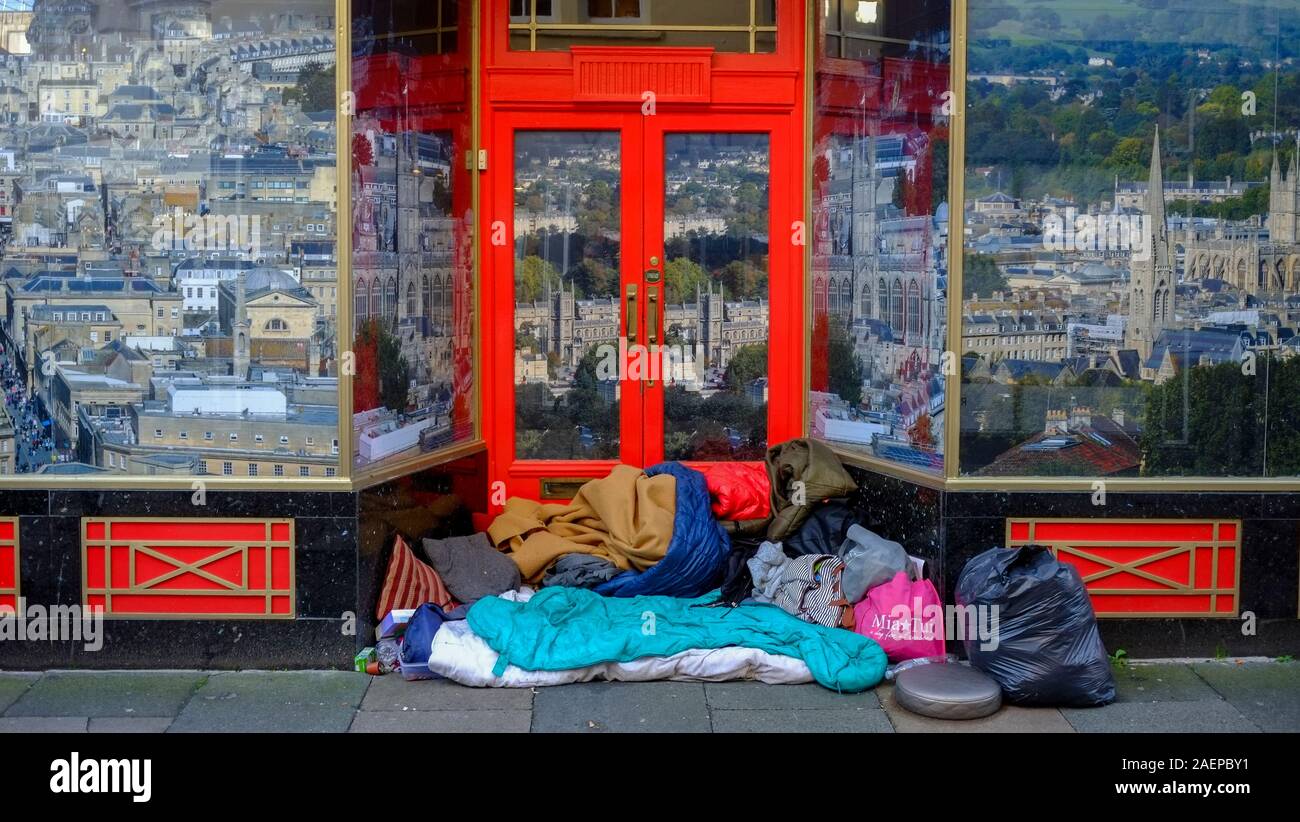 Un sans-abri d'appoint dans un magasin porte à Bath, Somerset, Royaume-Uni. Les sans-abri, des gens à la rue et la mendicité dans les centres-villes. La ville de Bath peut être vu que des images dans les fenêtres de la boutique. Banque D'Images