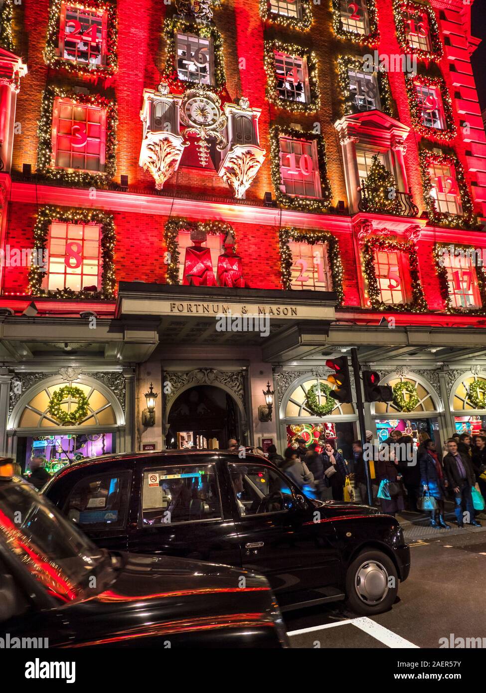 Fortnum & Mason Noël department store façade, avec un calendrier de l'avent rouge nuit à thème très occupé avec les acheteurs de Noël, les taxis noirs de Londres en premier plan Piccadilly Londres UK 2019 Banque D'Images