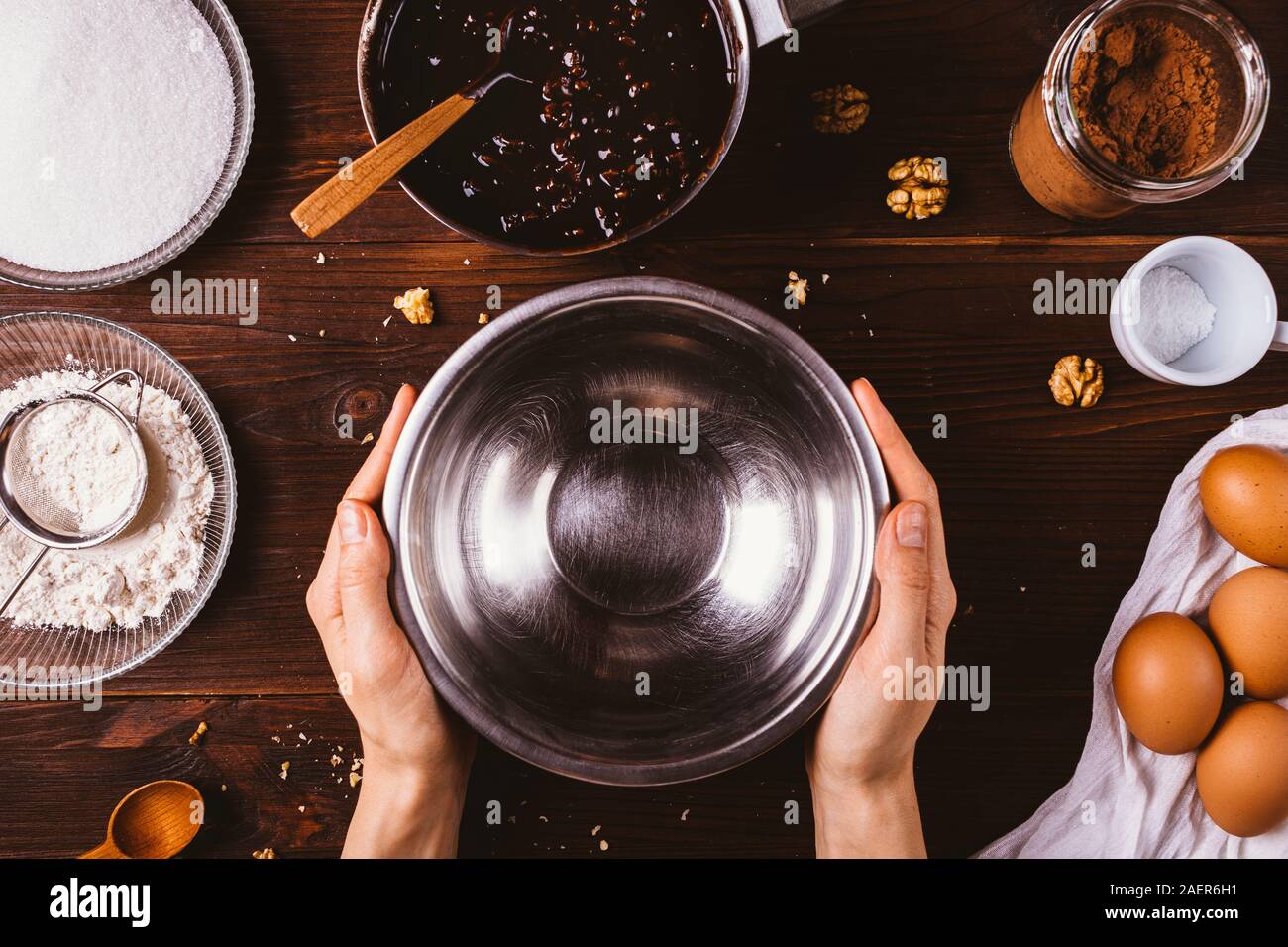 Femme's hands holding empty bol en métal pour faire de la pâte à brownie fait maison à base de chocolat fondu, la farine, le cacao, les oeufs et le sucre sur ta cuisine sombre Banque D'Images