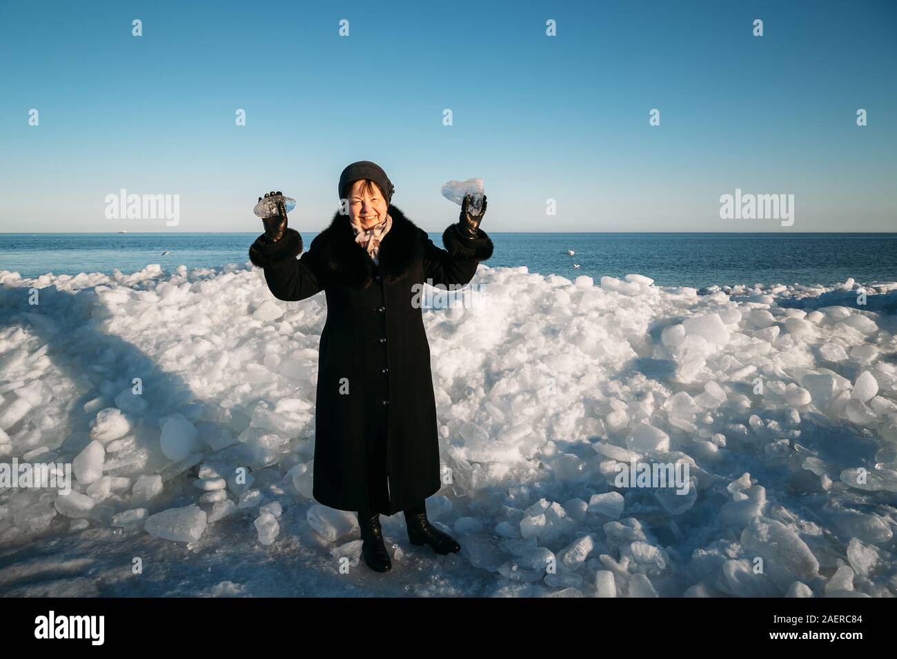 Smiling Senior woman in black coat holding morceaux cassés de la glace de mer debout devant la glace en bosses Banque D'Images