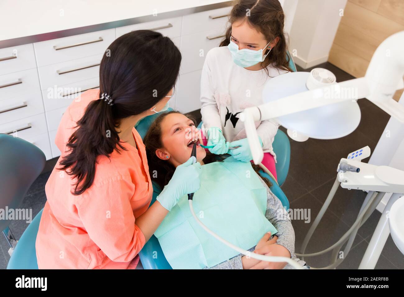 Adorables enfants dentiste en chirurgie dentaire avec deux jolies jeunes filles en leur montrant examen dentaire, une fille est à l'assistant Banque D'Images