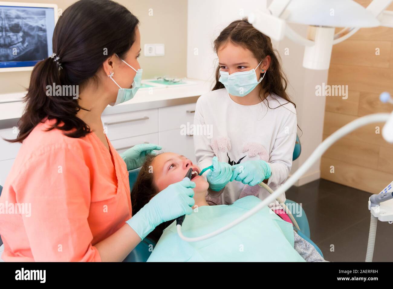 Adorables enfants dentiste en chirurgie dentaire avec deux jolies jeunes filles en leur montrant examen dentaire, une fille est à l'assistant Banque D'Images