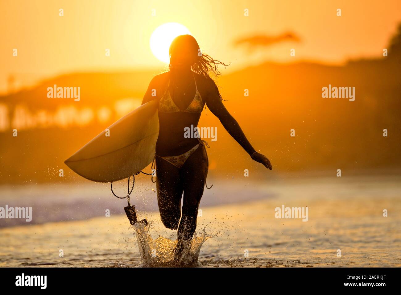 Fille courir le long du bord de l'eau transportant surfboard, El Salvador. Banque D'Images