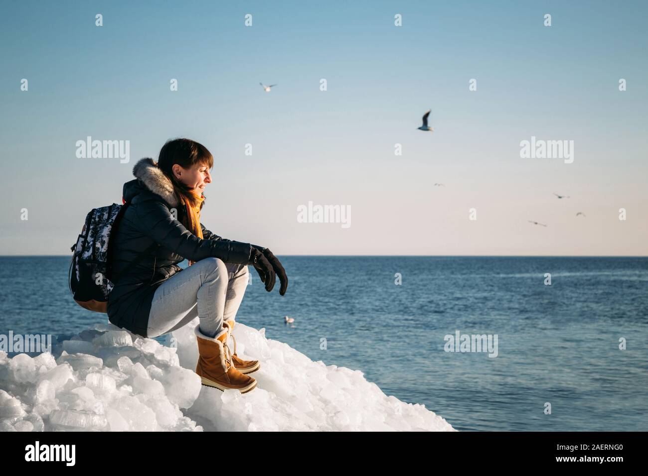 Young smiling woman sitting on a haut de la glace de mer congelés blocs sur une côte de la mer, avec un ciel bleu à l'arrière-plan, à frosty journée ensoleillée Banque D'Images