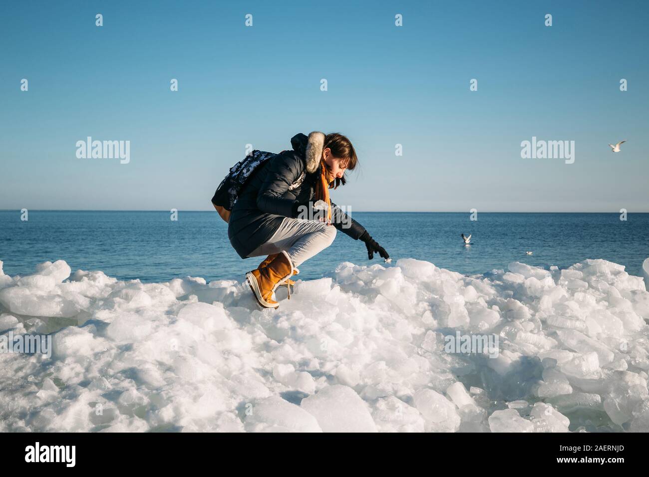 Young smiling woman sitting sur le dessus de la glace de mer bloque sur la côte holding broken morceau de glace, avec une mer bleue et le ciel et l'arrière-plan Banque D'Images