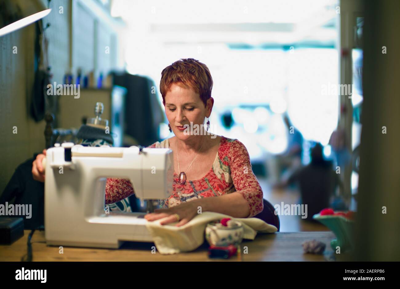 Femelle adulte couturière fabrication de vêtements tout en restant assis à une machine à coudre à l'intérieur de son magasin. Banque D'Images