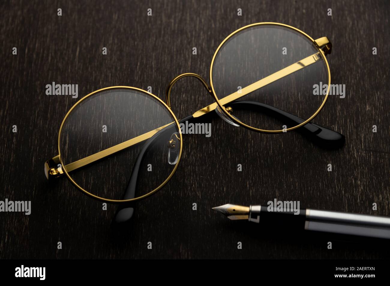 Lunettes d'or, la plume sur un fond de bois foncé.. Banque D'Images