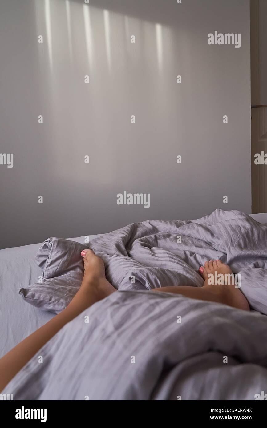 Libre les jambes des femmes sont en beige literie en chambre cosy. Matin tranquille et paresseux, concept copie espace vertical, Banque D'Images