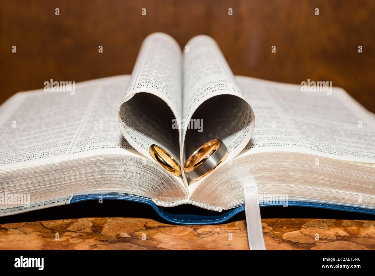 Ouvrir un livre de la bible avec pages recroquevillée dans un coeur et les anneaux de mariage. Banque D'Images