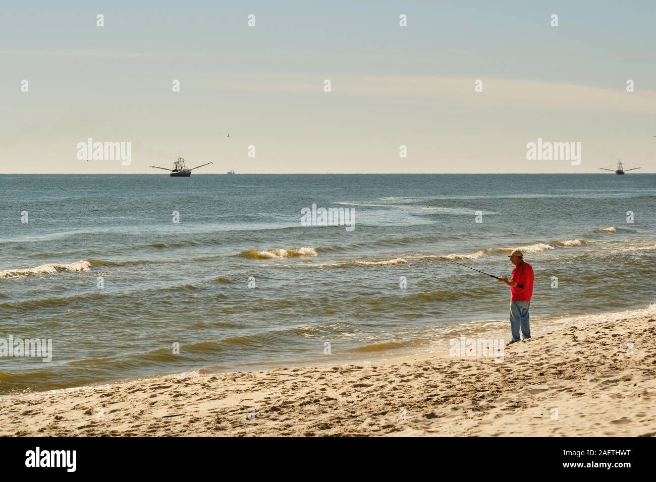 L'homme la pêche dans le golfe du Mexique sur Dauphin Island avec bateaux de crevettes à l'arrière-plan, sur l'Île Dauphin Alabama, Etats-Unis. Banque D'Images