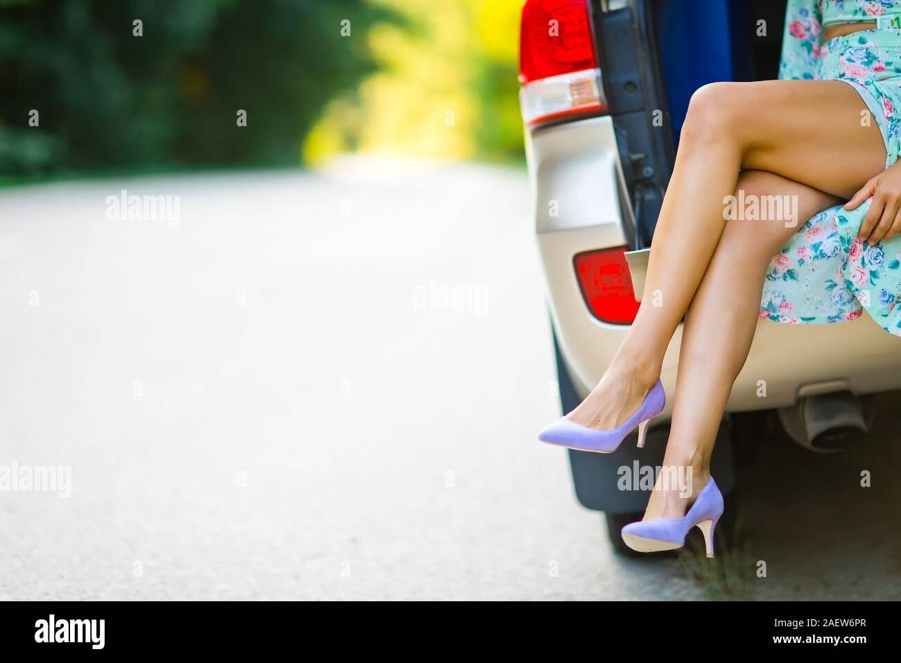 Séduisante prostituée avec des jambes assis dans coffre de voiture, porter des chaussures de talon Banque D'Images