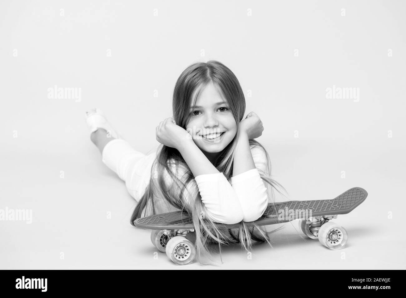 Petite fille sourire avec skate board sur fond rose. Patineur Enfant souriant de longboard. Skateboard kid se trouvent sur le sol. Vie de l'enfance et des jeux actifs. L'activité sportive et de l'énergie, punchy pastel. Banque D'Images