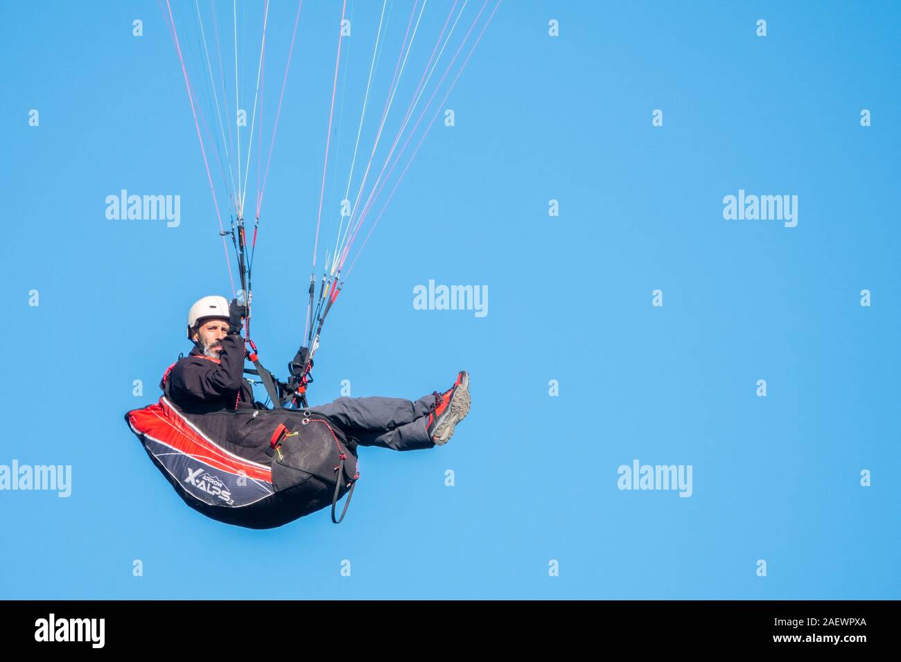 Homme barbu assis dans un banc de parapente en vol, full frame blue sky background, looking at camera with copy space Banque D'Images