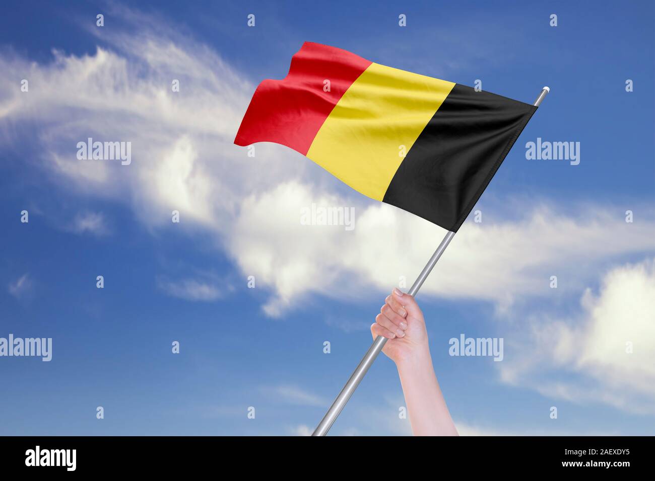 Main femme brandit le drapeau de la Belgique contre le ciel bleu avec des nuages. Des reflets réalistes et des textures à haute résolution. Le rendu 3D. Banque D'Images