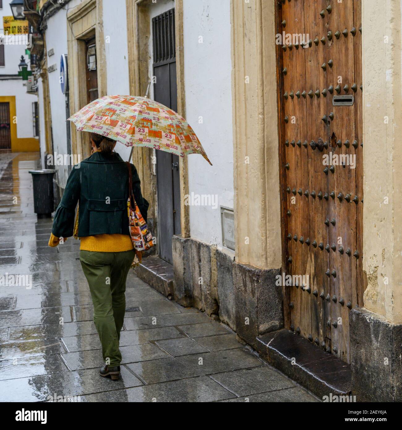 Vue arrière d'une femme marchant le long de la vieille ville ruelle dans la pluie, département de Córdoba, Córdoba Centro, Province, Espagne Banque D'Images