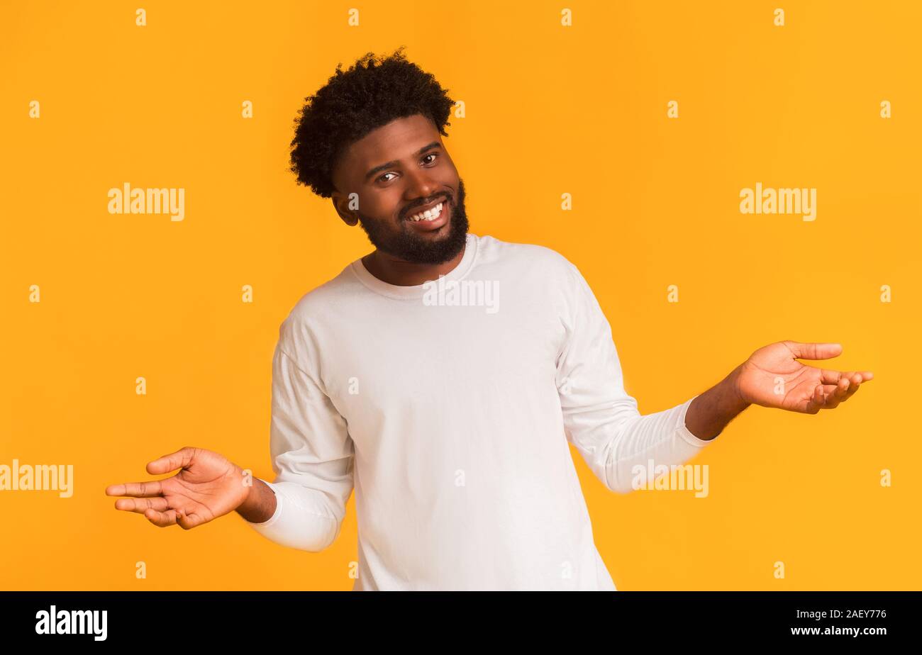 Jeune homme noir joyeux friendly smiling sur fond orange avec les bras ouverts, l'espace libre Banque D'Images