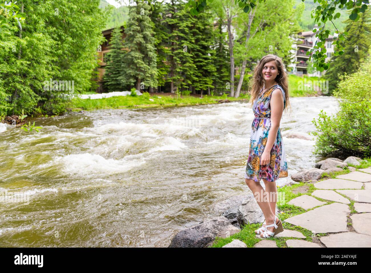 Jeune femme happy girl looking over Shoulder standing in Vail, Colorado, USA European style resort town par Gore Creek l'eau de rivière en été Banque D'Images