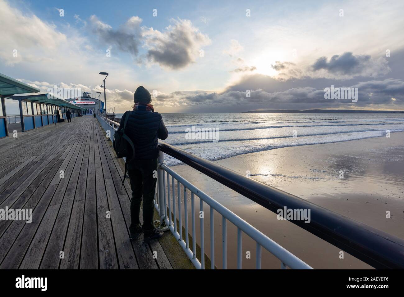 En hiver, de Bournemouth Dorset, UK, décembre 2019. Froid avec des averses de pluie, ensoleillée, avec un vent fort sur la côte sud de l'après-midi. Soleil et nuages orageux sur l'île de Purbeck et hardy les gens sur le quai en manteaux d'hiver. Banque D'Images