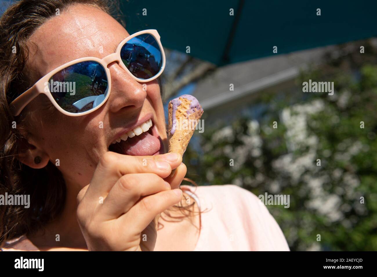 Une jeune femme en chemise rose de lécher les gouttes d'un cornet de crème glacée de fusion. Banque D'Images
