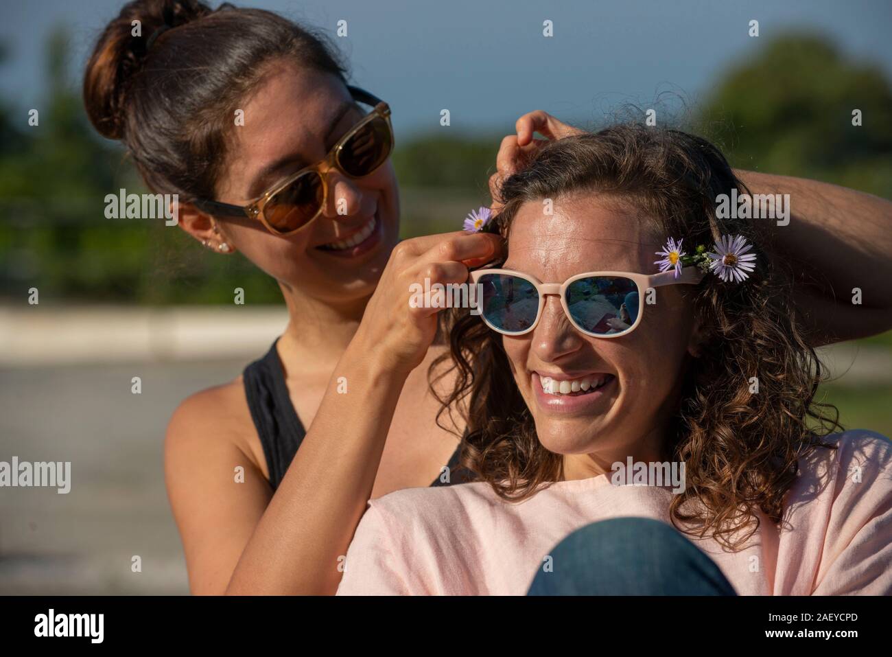 Deux femmes à l'extérieur de rire et de mettre des fleurs dans les cheveux. Banque D'Images