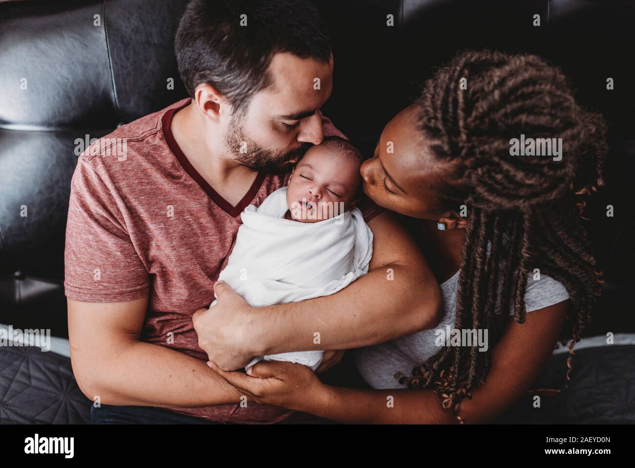 Les parents s'embrasser multiraciale bébé nouveau-né enveloppé dans une couverture blanche Banque D'Images