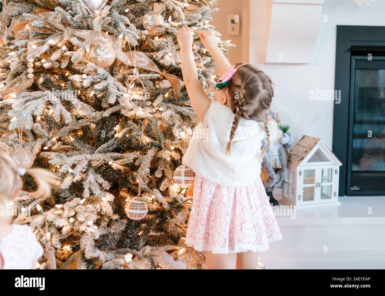 Tout-petit en robe rose mettre un ornement sur un arbre de Noël floqué Banque D'Images