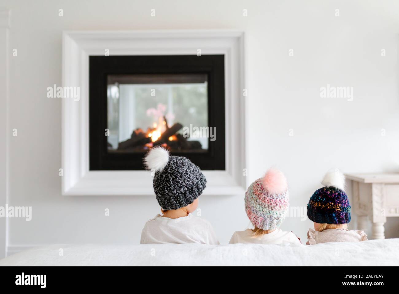Les tout-petits assis en face d'une cheminée avec toque knit hats Banque D'Images