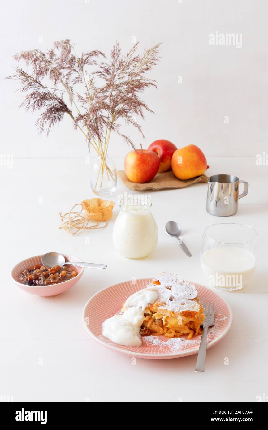 Table en bois blanc avec apple pain et beurre au lait, pot de crème sure, verre de lait, fond décoré avec quelques pommes et vase avec dry gra Banque D'Images