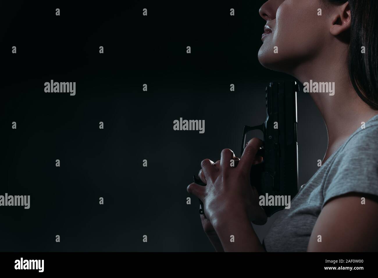 Portrait de femme déprimée holding gun près de menton sur fond sombre Banque D'Images