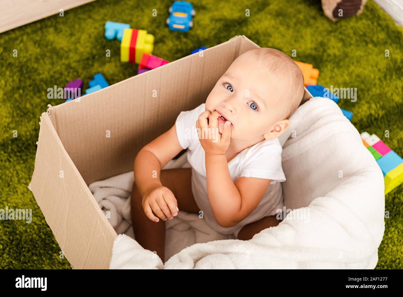 Cute blue-eyed enfant assis dans la boîte en carton avec couverture blanche sur marbre vert Banque D'Images